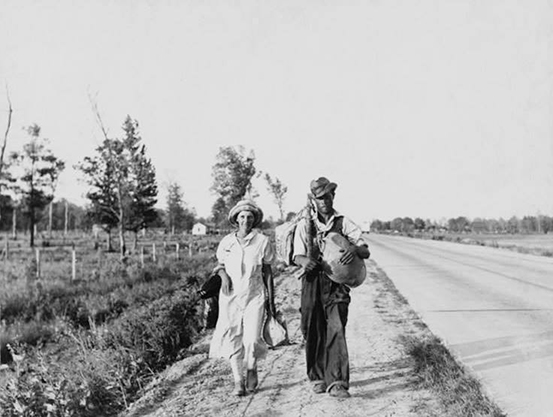 Black and white photo of a man and woman walking along the side of the road.
